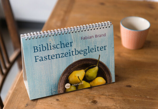 Biblischer Fastenzeitbegleiter steht auf einem alten Holztisch neben einer orange gestreiften Tasse