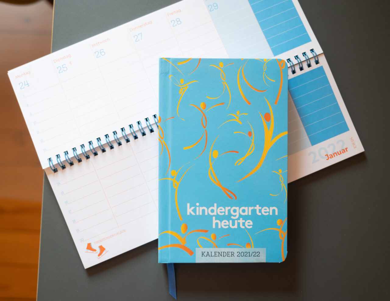 Produktfoto Kindergarten heute Tischkalender und Taschenkalender in Blau mit orangenen Figuren auf dem Cover