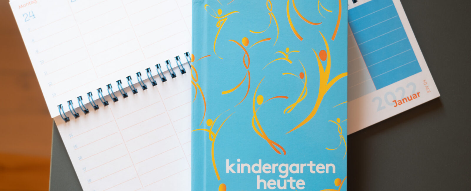 Produktfoto Kindergarten heute Tischkalender und Taschenkalender in Blau mit orangenen Figuren auf dem Cover